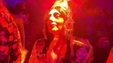 Büyük tüylü, gözlüklü, kostüm danslı güzel bir kadın saçlarını düzeltiyor, kırmızı ışık müzik partisi Kleopatra Cadılar Bayramı kostüm partisi gemisi Virgin Voyage France Cannes France Cannes 10.31.2024