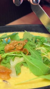 Mantarlı yumurta güveci ve bıçak ve çatallı roka kadın öğle yemeği için lezzetli bir parça peynir kesiyor. Yüksek kalite 4k görüntü