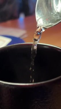 Koyu kahve fincanına sıcak kahve doldurmak, sabah vakti eski ahşap masaya bardak koymak, dumanı tüten sıcak kahveyi yakın çekim yapmak, ağır çekim. Sıcak içecek konsepti. Yüksek kalite 4k görüntü