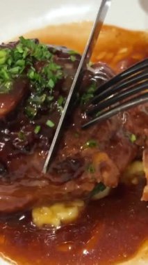 Eklem çatal ve bıçakla yenir. Jambon budu. Bir adamın eli, iştah açıcı bir et tabağını kemiğe bıçakla keser. Garnitürlü et yemeği hazır. Ahşap bir arka planda boğum. Pişmiş Eisbein.