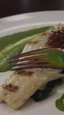 Patates püresi ve sebzeyle süslenmiş kızarmış beyaz balık parçası yeşil tabakta ve beyaz arka planda dönüyor. Soslu levrek. Restoran ana yemek konsepti. Üst Görünüm.