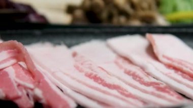 Şef kızartma tavasının yüzeyine taze domuz pastırması dilimleri koyar. Çiğ domuz pastırması ızgara tavada kızartılıyor. Pastırmalı pastırmalı pastırma kızartması. Yüksek kalite 4k görüntü