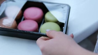 Karton kutuda pişmiş çok renkli badem kurabiyeleri, kadın eli tatlıyı alır, üst manzara. Yüksek kalite 4k görüntü