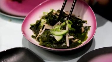 Yakın plan kadın eli Çin ahşap çubuklu deniz yosunu salatası alır. Deniz ürünleri sağlıklı yemektir. Taze deniz yosunundan lezzetli ve sağlıklı vegan yemekleri konsepti. Salatalıklı yosun