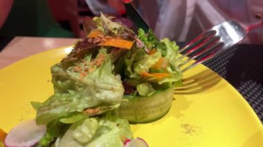 Salatalık, havuç turpu ve marul yapraklı salata. Kadın, çatal, kırmızı manikür ve bıçakla bir parçayı kesiyor. Yüksek kalite 4k görüntü