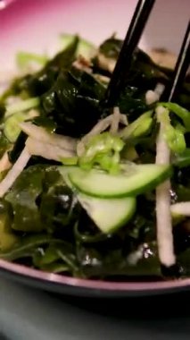 Yakın plan kadın eli Çin ahşap çubuklu deniz yosunu salatası alır. Deniz ürünleri sağlıklı yemektir. Taze deniz yosunundan lezzetli ve sağlıklı vegan yemekleri konsepti. Salatalıklı yosun