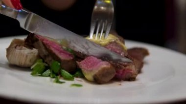 Taze ızgara biftek parçaları siyah arka planda bir çatalla döner, yeşil maydanoz sosu döker. Yiyeceğe yakın çekim. Yüksek kalite 4k görüntü