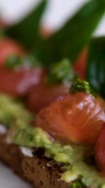 Avokado tostu ve kuru domatesler yukarıdan çekiliyor. Egzotik vejetaryen kahvaltı menüsüyle video klipsi açılıp vejetaryen kafe masasındaki geri dönüşümlü kağıtta servis ediliyor. Lezzetli öğle yemeği görüntüleri yakınlaştırıyor.