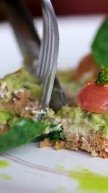 Çatal ve bıçaklı avokado tostuyla yemek küçük kiraz domatesleri ve fesleğen yaprağı süslemeleri. Yüksek kalite 4k görüntü