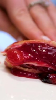 Meyvelerle dolu küçük bir kurabiye turtası beyaz bir tabağın üzerinde duruyor. Bir bıçak kiraz dolu bir keki parçalara ayırır. Tahta bir yüzeyde ev yapımı meyveli tart. sstkdikey video.