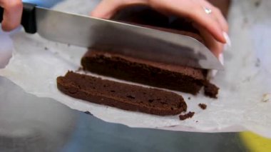 Fırıncı çikolatalı keki bıçakla küçük parçalara ayırıyor ve şeffaf yerel fırın giyiyor. - Evet. Yüksek kalite 4k görüntü