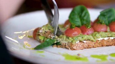 Çatal ve bıçaklı avokado tostuyla yemek küçük kiraz domatesleri ve fesleğen yaprağı süslemeleri. Yüksek kalite 4k görüntü
