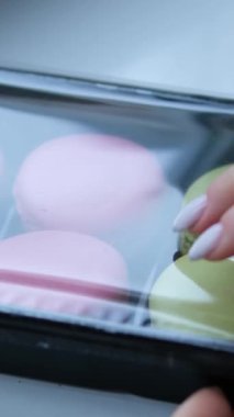 Karton kutuda pişmiş çok renkli badem kurabiyeleri, kadın eli tatlıyı alır, üst manzara. Yüksek kalite 4k görüntü