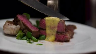 Şef, ahşap kesme tahtasına taze ızgara biftek eti dilimlerinin üzerine biber sosu döker. Yemeklere yakın çekim, manzaralı. Yüksek kalite 4k görüntü