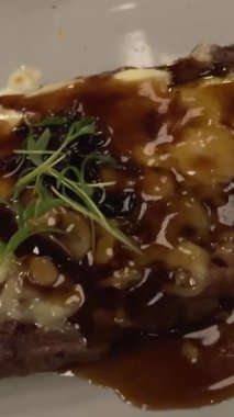 Gece karanlık bir restoranda, beyaz tabakta soslu az pişmiş bir biftek. Yüksek kalite 4k görüntü