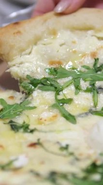Zeytin, roka, jambon ve erimiş peynirle kaplı bir dilim pizzayı tutan bir el parşömen kağıdında servis edilir. Lezzetli bir aperatif veya yemek için mükemmeldir. Yüksek kalite 4k görüntü