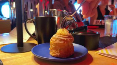 Seçici odak Cromboloni, ahududu ezmesi ile servis edilen Bombolonili kruvasan ekmekli kek. Viral tatlı ekmeği Endonezyası. siyah fincan mavi tabak yuvarlak kruvasan kesimi kaşık ile