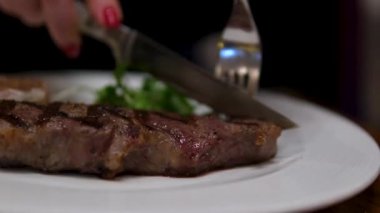Kesme tahtasındaki büyük bir mutfak bıçağıyla bifteği kesme işleminin dikey görüntüleri. Sulu sığır eti parçalara ayrılmış. Şefin elinin yakın çekimi, ağır çekim. Yüksek kalite 4k görüntü
