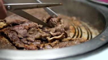 Kore usulü ızgara domuz eti pişirirken yakın çekim ve ızgarada et kesmek için makas kullanın. Izgarada domuz göbeği, tavada domuz eti pişirme, Kore usulü barbekü. Yüksek 