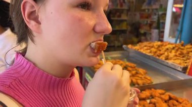 Chatuchak pazarı, tezgâhtar kızın üzerinde Tayland usulü ızgara domuz eti tadıyor. 04.05.2025