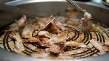 Et dilimleri sıcak metal ızgarada cızırdıyor. Makas eti küçük parçalara ayırıyor. Masanın etrafında Kore tarzı garnitürler var. Ev yemeği ortamı. 4K 60fps. Yüksek kalite 4k görüntü