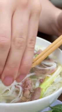 Bir el Bangkok 'un hareketli restoranlarında bir kase pho' nun üzerine limon sıkıyor, bulaşık tadını arttırıyor. Yüksek kalite 4k görüntü