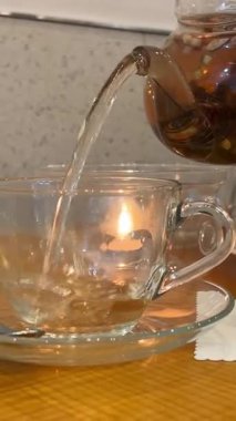 Yeşil bluz ve beyaz önlük giymiş ev hanımı huzurlu bir sabah boyunca çiçekli, pastalı ve klasik kitaplı rahat mutfak masasında şeffaf cam bardağa bitki çayı döküyor. 