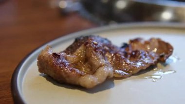 Açık ızgara ve kömürlü Kore restoranı usulü barbekü. Çeşitli et kesimleri manipüle ediliyor, kesiliyor ve pişiriliyor. Beyaz duman yukarıdaki egzoz dumanına doğru yükseliyor..