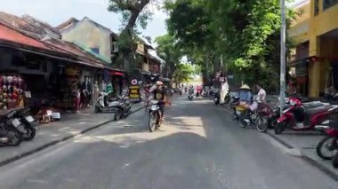 Bisikletli ve arabalı insanların yanından geçerken yolu çek. Vietnam Hoi 'nin merkez caddesi. 05.20.2025.