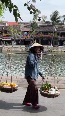 Elinde boyunduruğu ve meyvesi olan bir kadın gelip geçenlere ağır bir sepete dokunmayı teklif ediyor sonra da para istiyor ya da Vietnam 'da para için meyve almak istiyor.