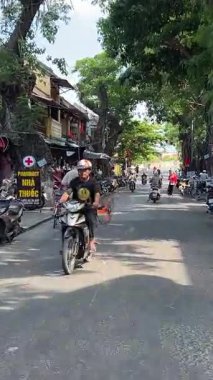 Bisikletli ve arabalı insanların yanından geçerken yolu çek. Vietnam Hoi 'nin merkez caddesi. 05.20.2025.
