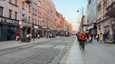 İnsanlar ana cadde boyunca yürür. Kameranın önünden kırmızı bir tramvay geçiyor. Polonya Katowice 06.20.2025