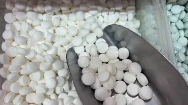 Çeşitli beyaz yuvarlak tabletler yığını, uzun kapsüller, ve koyu ahşap bir yüzeye saçılmış şeffaf softgel haplar, yan ışıklandırma hatları vurguluyor, pullu puan