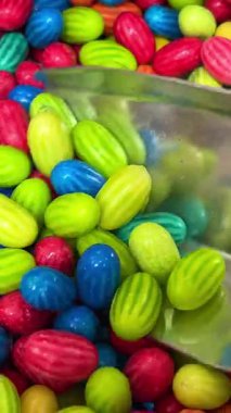 Parlak renkli jelibonların arka plandaki videosu, ahşap kaşık gelir ve biraz şeker toplar. Yüksek kalite 4k görüntü