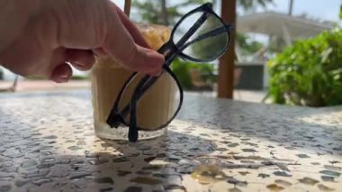 Kız, tropik bölgelerde latte kötü görüş düzeltme tatilinin yakınındaki masaya gözlük koyuyor. Yüksek kalite 4k görüntü