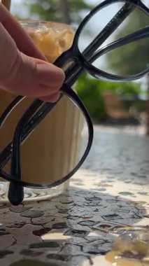 Kız, tropik bölgelerde latte kötü görüş düzeltme tatilinin yakınındaki masaya gözlük koyuyor. Yüksek kalite 4k görüntü