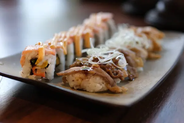 Karışık suşi rulosu ve sashimi tabağı. Yumuşak odaklı görüntü. Suşi ve sığır eti, kızarmış et ve ızgara somon balığı, somon balığı, Asya mutfağı deneyleri.