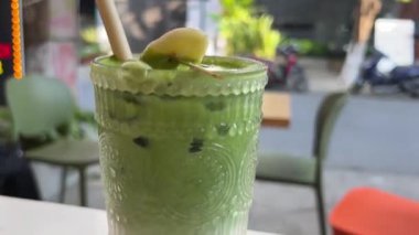 Taze yapılmış yeşil ıspanak ve muz suyu güneşli bir masa yüzeyindeki bir şişeden bir bardağa akıyor. Yüksek kalite 4k görüntü