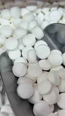 Çeşitli beyaz yuvarlak tabletler yığını, uzun kapsüller, ve koyu ahşap bir yüzeye saçılmış şeffaf softgel haplar, yan ışıklandırma hatları vurguluyor, pullu puan