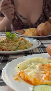 Güneşli bir günde otelde kahvaltı yapan bir kadın. Mavi yüzme havuzunun yanındaki villada sabah yemeği. Havuz başında yiyecek dolu bir masa, sağlıklı kahvaltı ve tatil beldeleri için meyve tabağı. Tropikal lüks yaşam tarzı