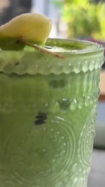 Taze yapılmış yeşil ıspanak ve muz suyu güneşli bir masa yüzeyindeki bir şişeden bir bardağa akıyor. Yüksek kalite 4k görüntü