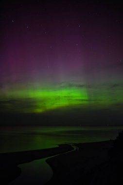 Muhteşem Kuzey Işıkları Baltık Denizi üzerinde dans ediyor, gece gökyüzünde canlı renkler bırakıyor ve aşağıdaki sakin sulara yansıyor.