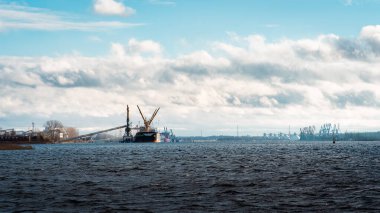 Arka planda dramatik bulutlar tarafından çerçevelenmiş iskele suya doğru uzanıyor, sakin ve atmosferik bir kıyı manzarası yaratıyor.