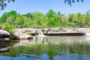 Sadece küçük bir şelalenin manzarası ağaçlar ve bitki örtüsüyle çevrili kayalar. Fotoğraf Austin Teksas 'taki McKinney Falls Eyalet Parkı' nda çekildi.