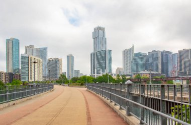 Gökdelen binalarıyla çevrili bir yaya yolu köprüsü. Fotoğraf Austin Texas şehir merkezinde bulutlu bir günde Lady Bird Gölü üzerindeki bir köprüde çekildi.