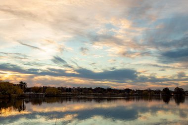 Dramatik günbatımı bulutları sakin ve huzurlu bir göle yansıyordu. Fotoğraf, San Antonio Teksas, Woodlawn Gölü 'ndeki ağaçlı ufuk boyunca çekildi.