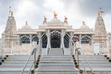 Ağaçlar ve suyla çevrili beyaz BAPS Shri Swaminarayan Mandir tapınağı. Fotoğraf bulutlu bir günde Houston Teksas 'ta çekildi.