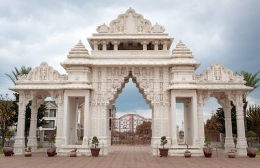 Elaborate white BAPS Shri Swaminarayan Mandir temple entrance gate. Photo taken in Houston Texas on a cloudy day clipart