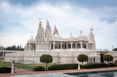 Ağaçlar ve suyla çevrili beyaz BAPS Shri Swaminarayan Mandir tapınağı. Fotoğraf bulutlu bir günde Houston Teksas 'ta çekildi.