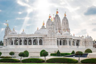 Ağaçlar ve suyla çevrili beyaz BAPS Shri Swaminarayan Mandir tapınağı. Fotoğraf bulutlu bir günde Houston Teksas 'ta çekildi.